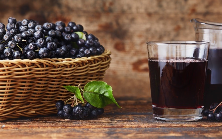 En kurv fyldt med aronia br str p et trbord, ved siden af et glas aronia juice.