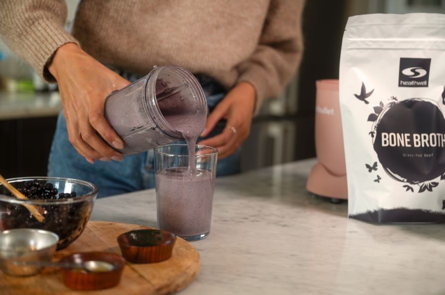 En kvinde h�lder en bl�b�r og bone broth smoothie op i et glas.