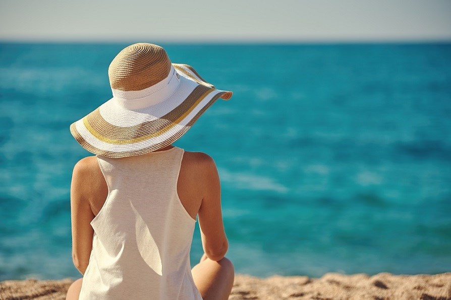 Kvinde med solhat og top, der sidder på en strand og kigger ud over havet. Kvinde med solhat og top, der sidder på en strand og kigger ud over havet.