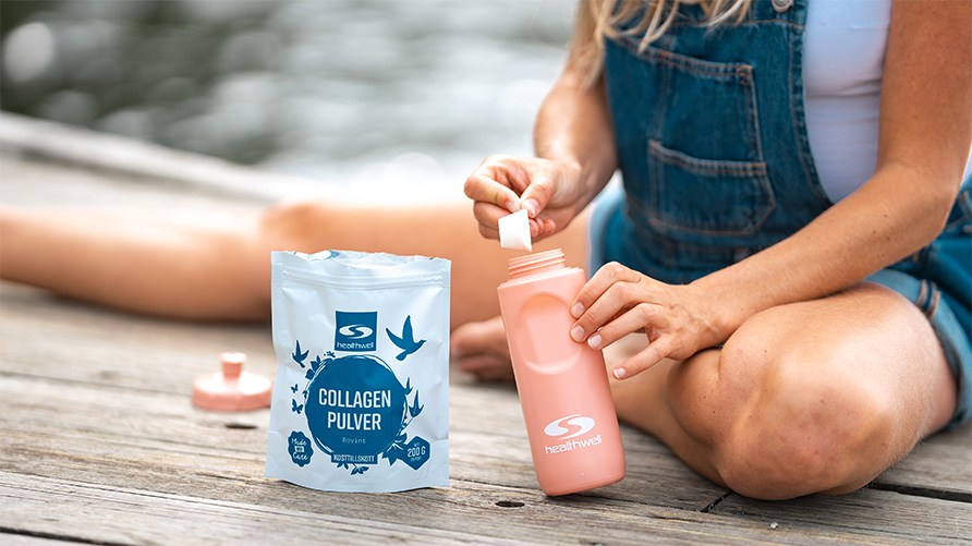 Kvinde sidder p� en badebro og tager en skefuld af Healthwell Collagen Pulver Bovint og h�lder det i en rosa vandflaske.