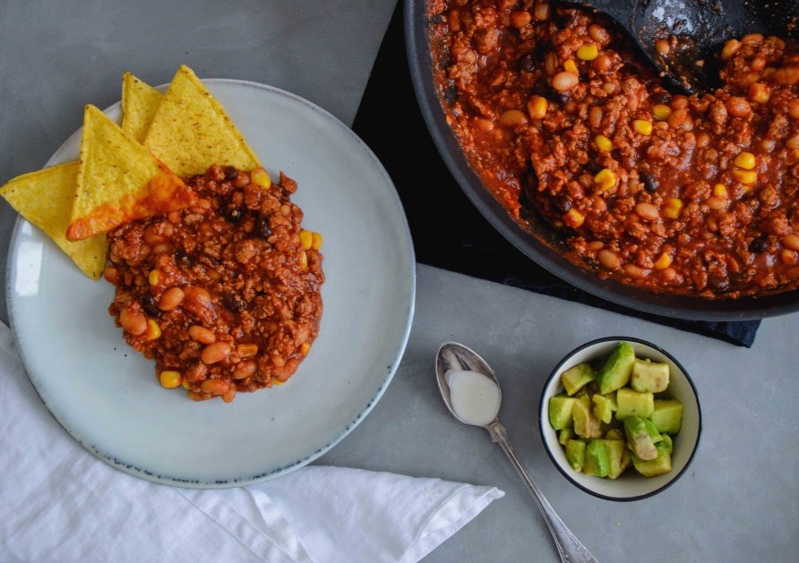 En tallerken med chili sin carne, hvor der er tilfjet nachos og ternet avocado.