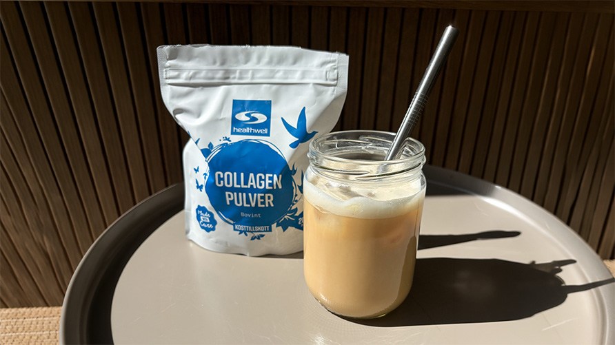 Et glas iced latte st�r p� et bord udend�rs sammen med en pose Healthwell Collagen Pulver Bovint.