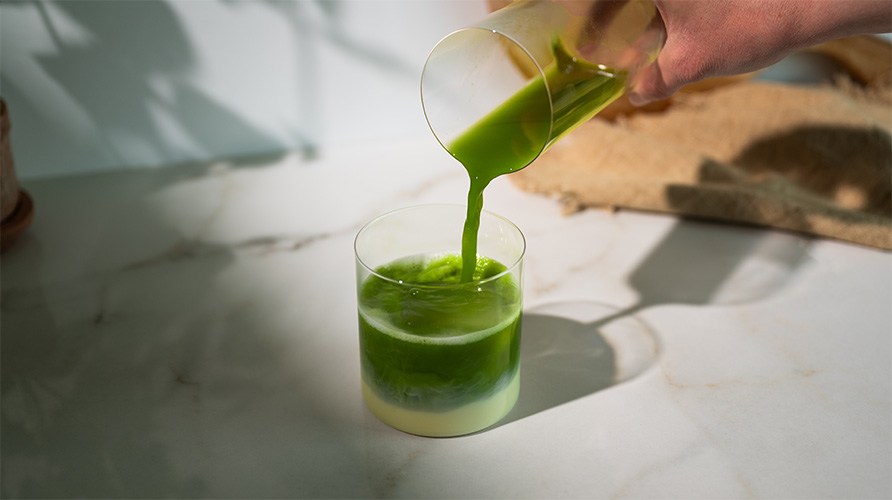 Person h�lder matcha i et glas med m�lk, is og blendet mango