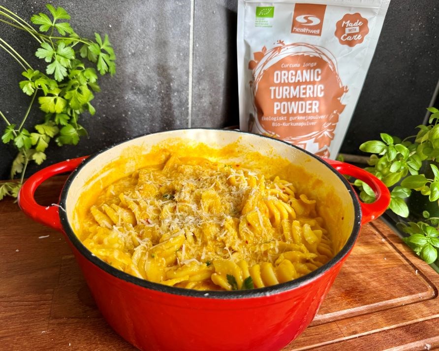 Kalorismarts kyllingegryde i en stor, rd gryde p en kkkenbnk af tr, og en pakning med Healthwell Gurkemeje Pulver KO.