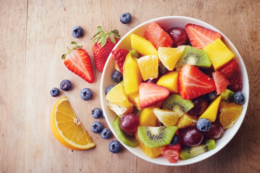 Frugter såsom kiwi, jordbær og appelsiner i stykker i en skål med blåbær ved siden af.