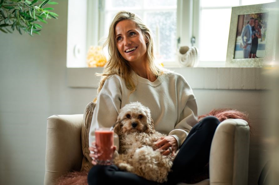 Lea Kessler sidder smilende i en lnestol med en smoothie og en hund.