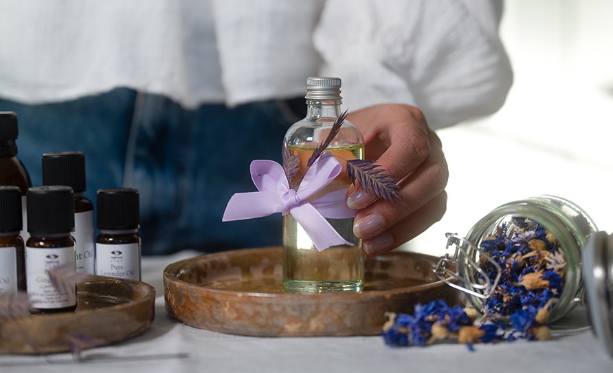 Kvinde, der griber en glasflaske med hjemmelavet massageolie i.