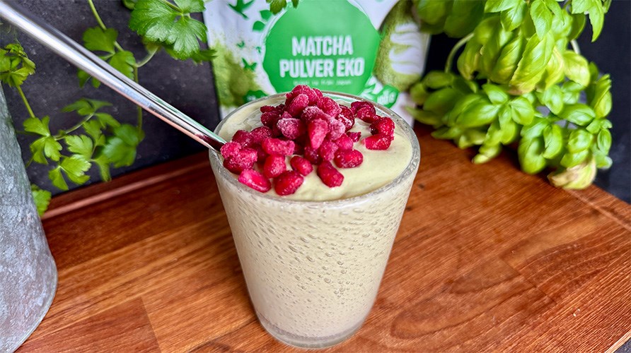 Healthwell Matcha Pulver EKO i originalemballage, Kalorismarts matchasmoothie i et glas toppet med br, potte og basilikum p et trbord.