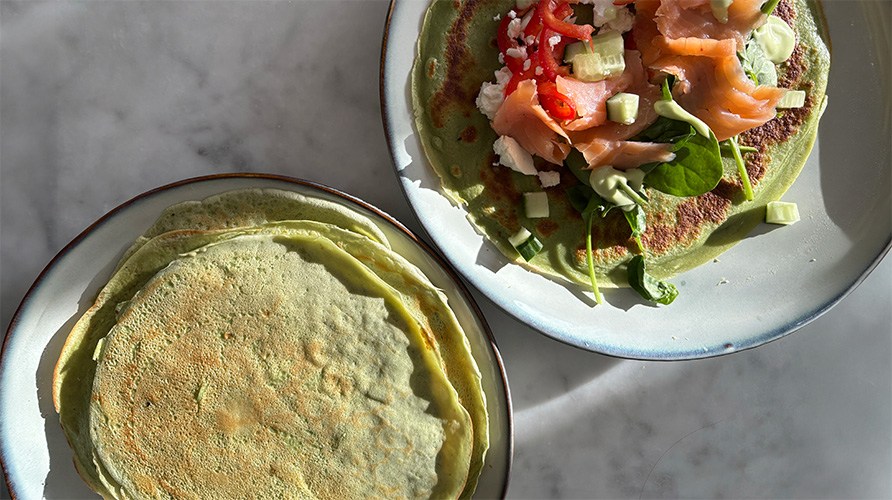 M�ttende pandekager med spirulina og moringa p� to tallerkener sammen med gravad laks, gr�ntsager og fetaost.