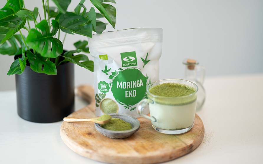 En trbakke med en kop moringalatte sammen med en pose Healthwell Moringa EKO.