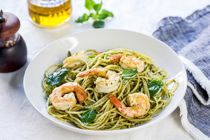 En dyb tallerken med rejepasta med pesto, stende p et bord.