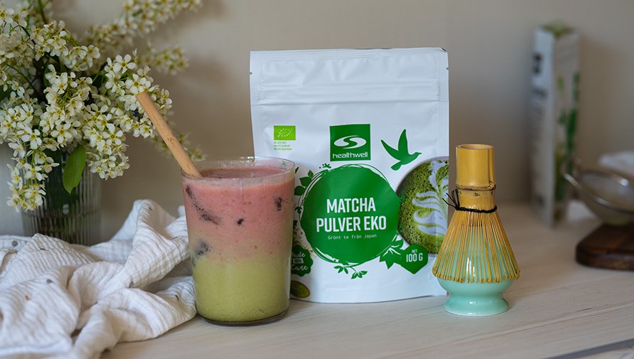 En iced strawberry matcha latte med et bambus sugerr og matcha piskeris.