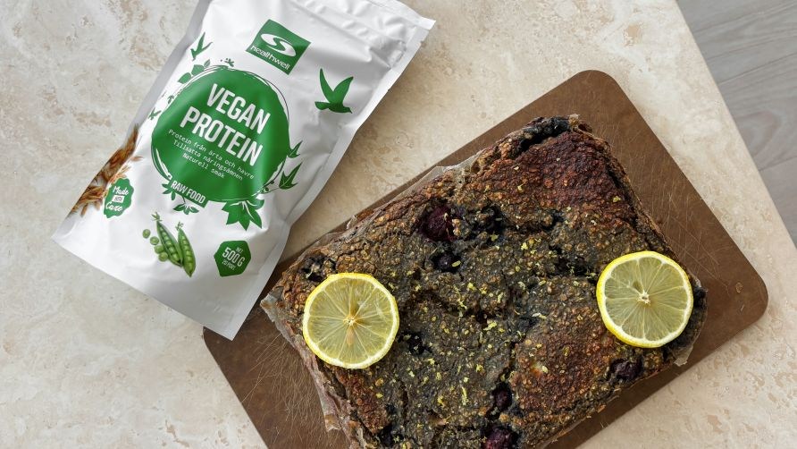 En pose Healthwell Vegan Protein ligger ved siden af veganske proteinbarer.