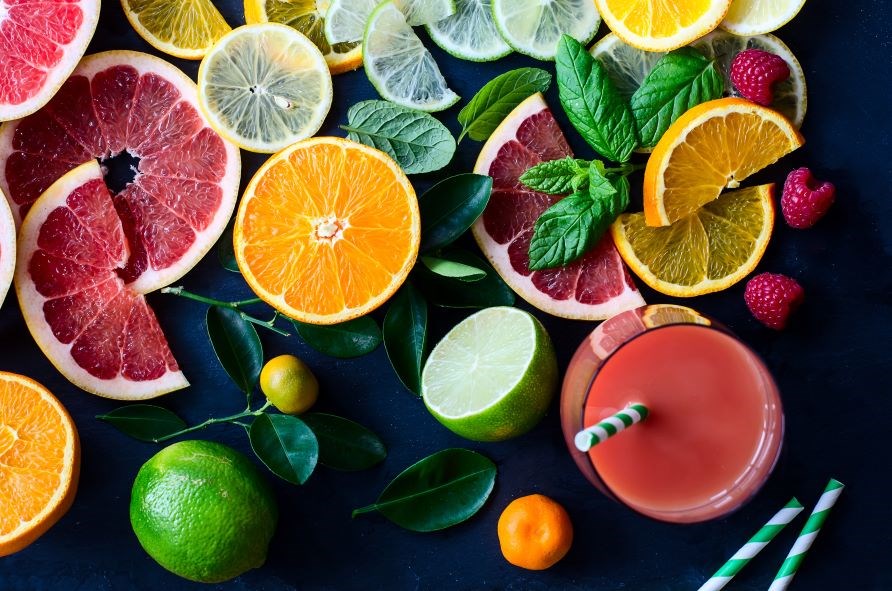 Citrusfrugter og et glas med smoothie p et mrkt bord.